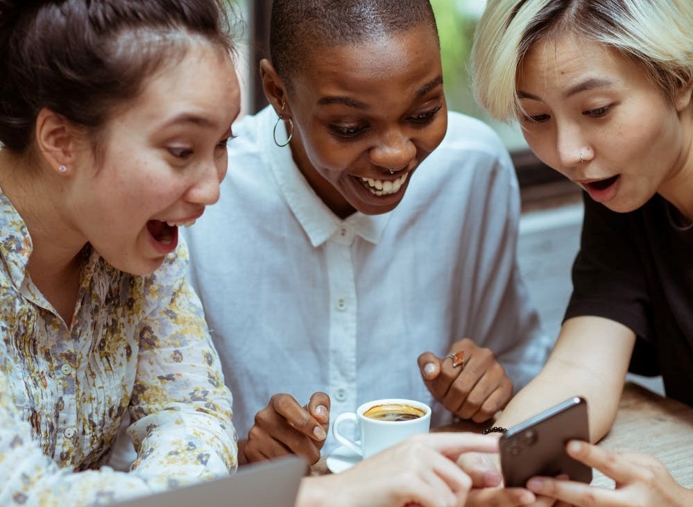 3 people smiling and pointing at a phone